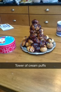 this is a plate of cream puffs covered in chocolate arranged in a tower on a wooden table